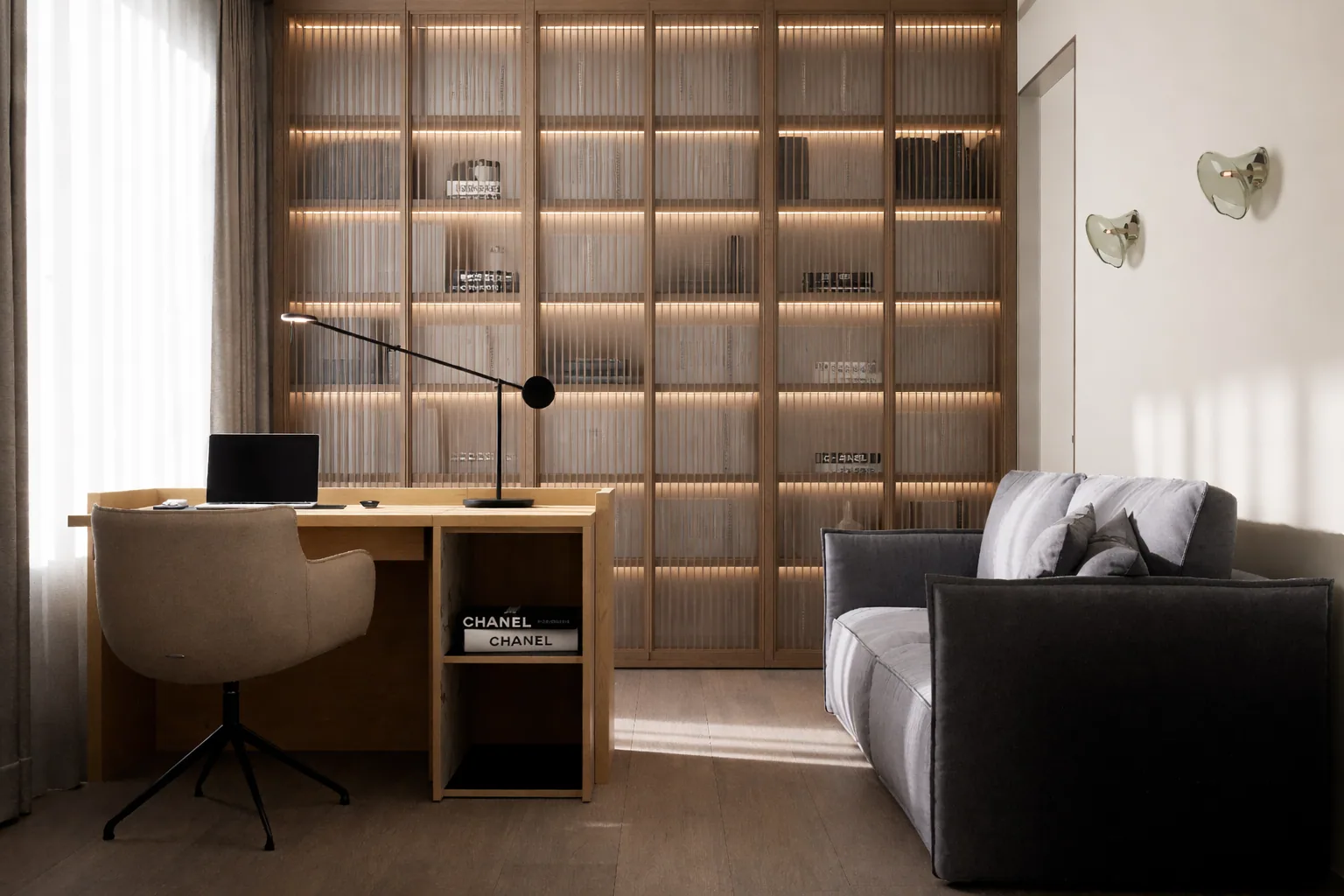 Home office with a wall of illuminated shelving and a compact sofa