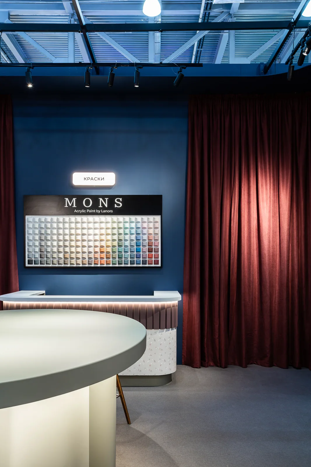 MONS colour display framed by a burgundy curtain inside the pavilion