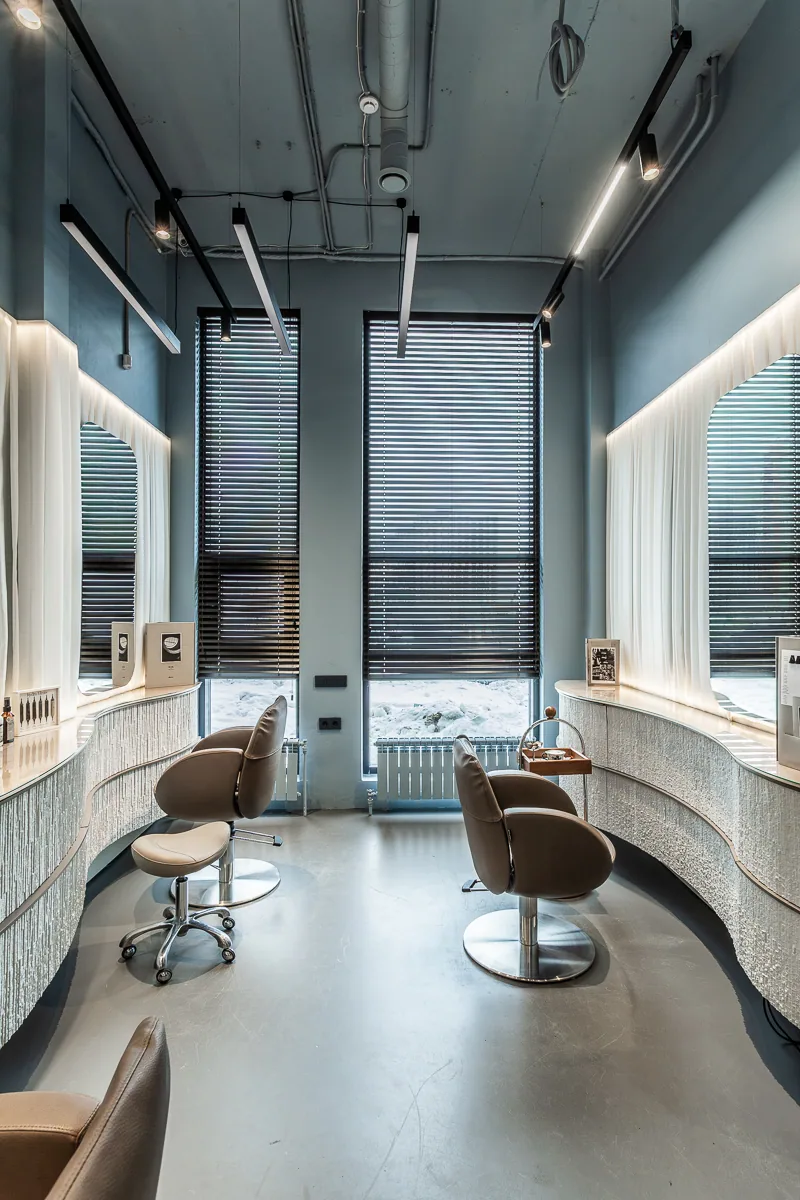 Hair styling chairs aligned along a curved wall beside tall windows